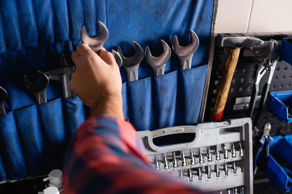 Ausgeschnittene Ansicht eines Mechanikers, der Schraubenschlüssel vom Set in der Nähe des Werkzeugkastens nimmt, verschwommener Vordergrund — Stockfoto