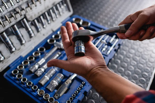 Ausgeschnittene Ansicht des Mechanikers, der Steckschlüssel in der Nähe des Werkzeugkastens auf verschwommenem Hintergrund hält — Stockfoto