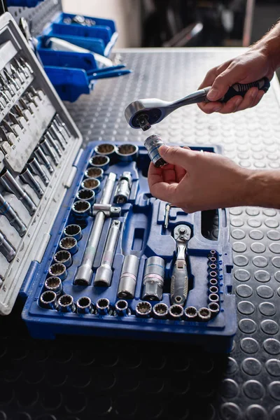 Vista recortada del reparador que sostiene la llave del enchufe cerca de la caja de herramientas en el taller - foto de stock