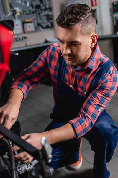 Meccanico in tuta da lavoro verifica moto in officina, primo piano sfocato — Foto stock