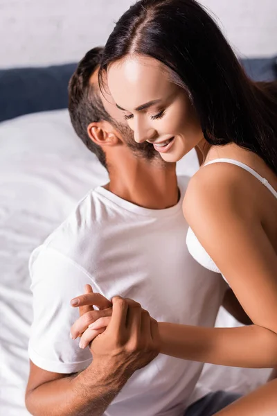 Happy brunette woman with closed eyes, holding hands with boyfriend on bed — Stock Photo