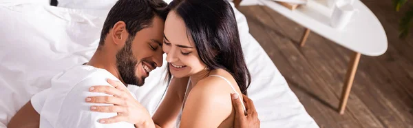 High angle view of young couple laughing while hugging on bed on blurred background, banner — Stock Photo