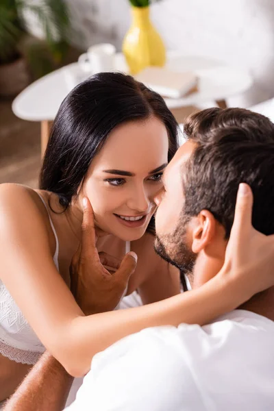 Sexy brunette woman in underwear smiling while looking at man indoors on blurred background — Stock Photo