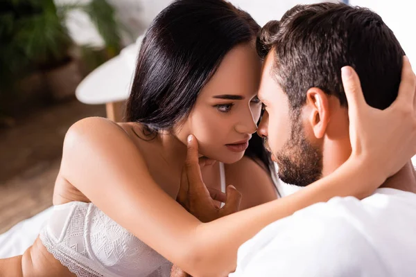 Passionate brunette woman in underwear looking at boyfriend on blurred background in bedroom — Stock Photo