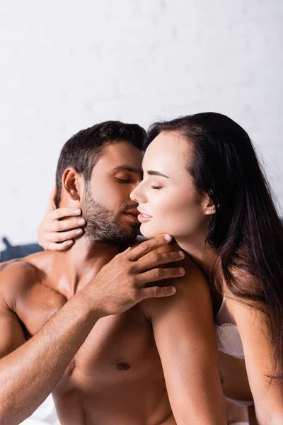 Sexy uomo senza maglietta toccare il viso della donna sensuale con gli occhi chiusi in camera da letto — Foto stock