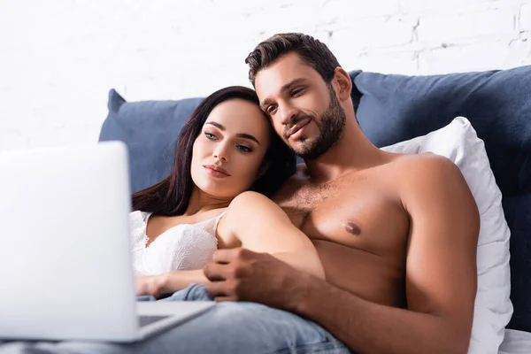 Junges sexy Paar blickt auf verschwommenen Laptop im Vordergrund im Schlafzimmer — Stockfoto