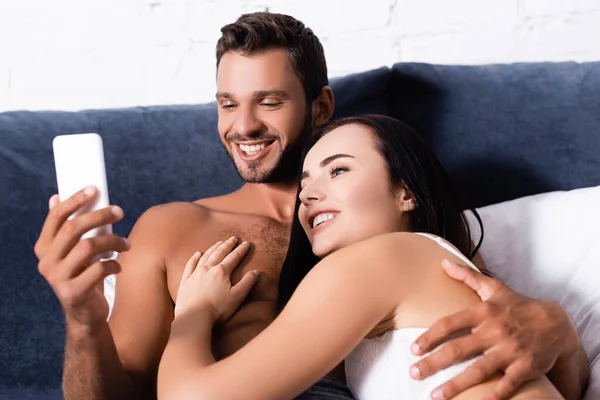 Happy young couple looking at smartphone while lying on bed — Stock Photo