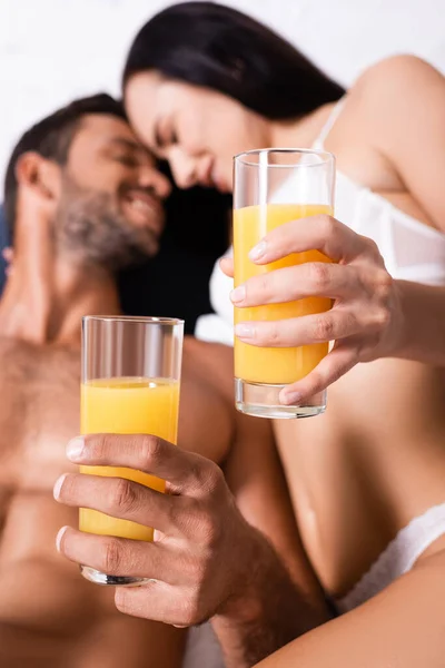 Close up vista de óculos com suco nas mãos de casal jovem sorridente no fundo borrado — Fotografia de Stock