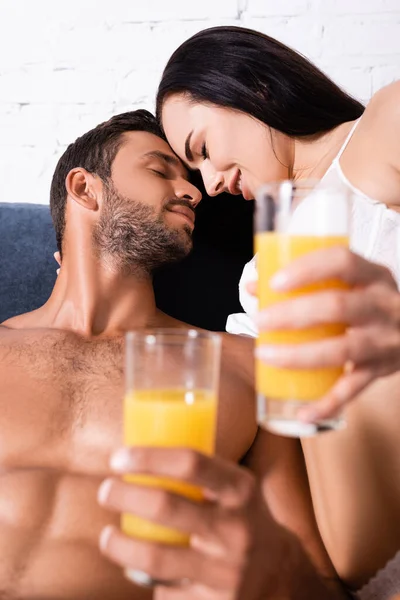 Sensual young couple with closed eyes holding blurred glasses of juice on foreground in bedroom — Stock Photo