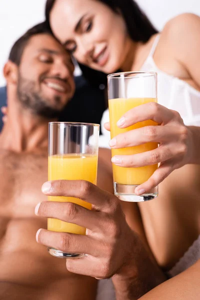 Close up vista de óculos com suco nas mãos de casal sexy feliz no quarto no fundo borrado — Fotografia de Stock