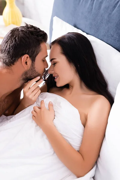 Smiling brunette woman with blanket looking at boyfriend on bed — Stock Photo