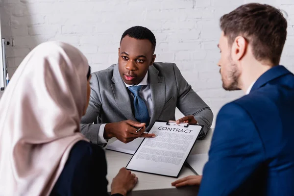 Homme d'affaires afro-américain pointant du doigt un contrat proche de partenaires d'affaires multiethniques sur un premier plan flou — Photo de stock