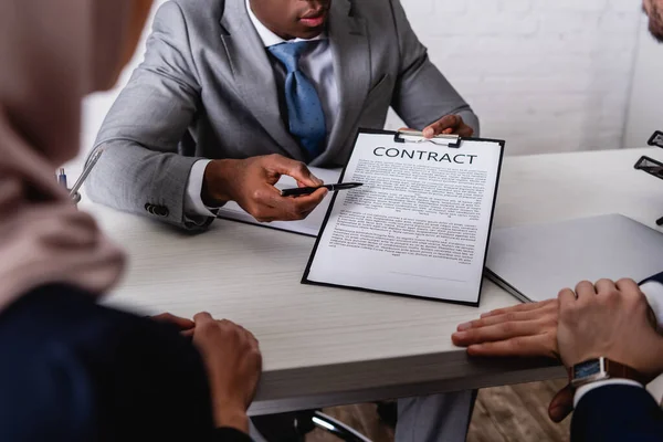 Partial view of african american businessman pointing at contract during negotiation with interracial business partners, blurred foreground — Stock Photo