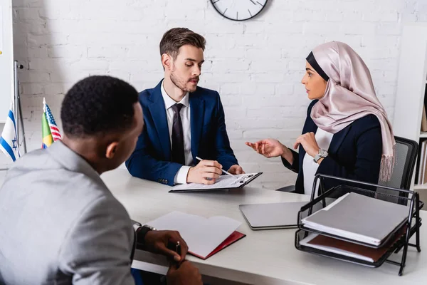 Geschäftsmann zeigt mit Stift auf Vertrag in der Nähe arabischer Geschäftsfrau und Dolmetscherin, verschwommener Vordergrund — Stockfoto