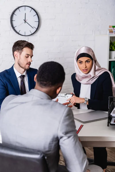 Arabian businesswoman pointing with finger at contract during meeting with interracial business partners, blurred foreground — Stock Photo