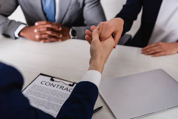 Selective focus of business partners shaking hands near contract and african american businessman, cropped view — Stock Photo