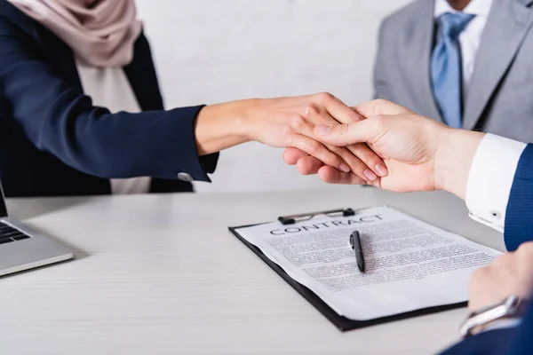 Cropped view of business partners shaking hands near contract, blurred background — Stock Photo