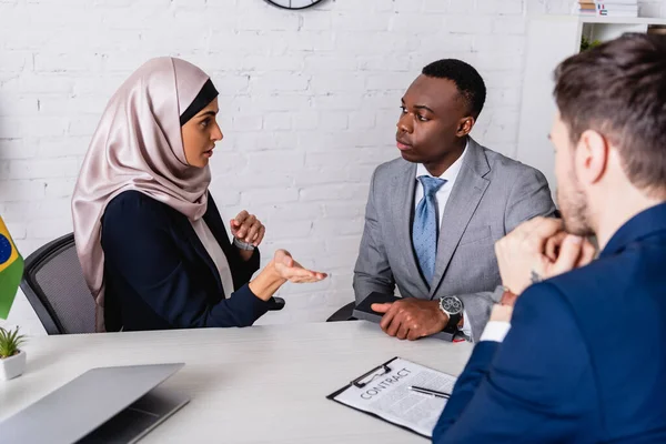 Arabe femme d'affaires pointant avec la main lors d'une réunion avec des partenaires commerciaux multiculturels près de contrat, flou premier plan — Photo de stock