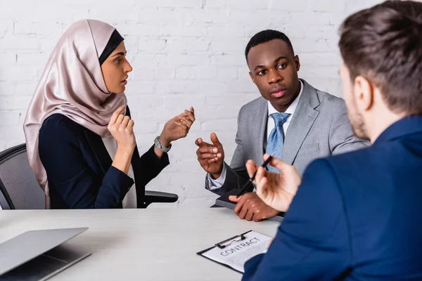 Multicultural businesspeople gesturing while discussing contract near interpreter, blurred foreground — Stock Photo