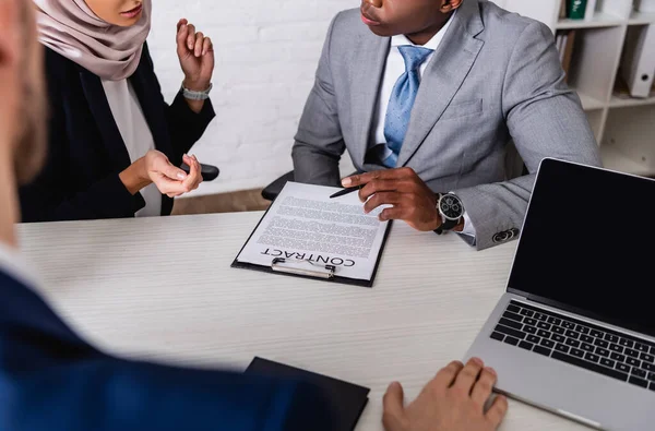 Geschnittene Ansicht eines afrikanisch-amerikanischen Geschäftsmannes, der während eines Treffens mit multiethnischen Partnern einen Stift in der Nähe des Vertrages hält, verschwommener Vordergrund — Stockfoto