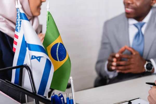 Selective focus of brazilian, american and uae flags near arabian and african american business partners on blurred background, cropped view — Stock Photo