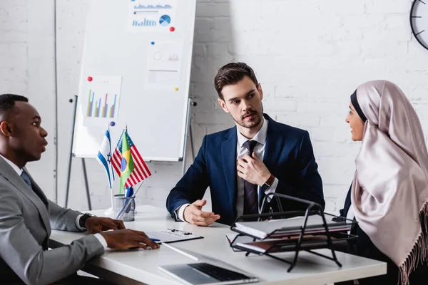 Traductor tocando la corbata durante reunión con socios de negocios afroamericanos y árabes — Stock Photo