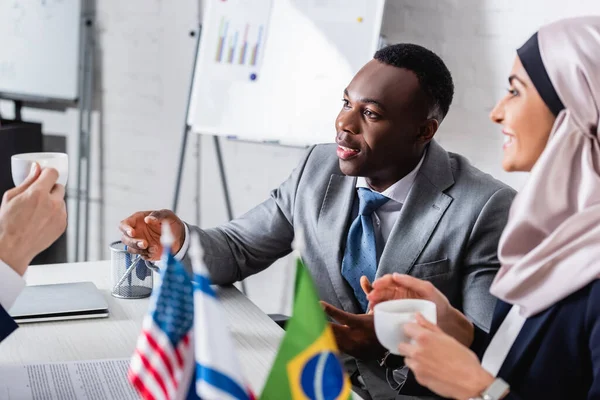 Afrikanisch-amerikanischer Geschäftsmann gestikuliert bei Treffen mit arabischem Geschäftspartner und Übersetzer, verschwommener Vordergrund — Stockfoto