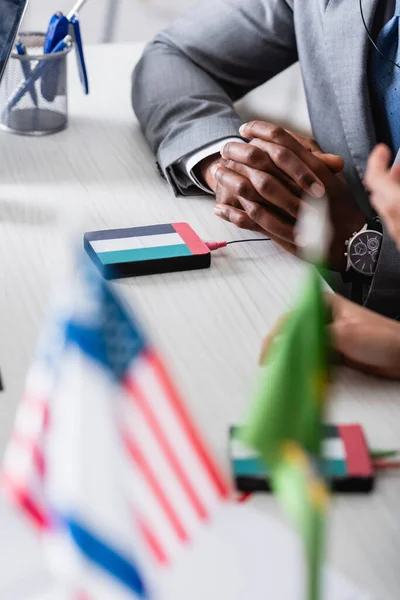 Abgeschnittene Ansicht eines afrikanisch-amerikanischen Geschäftsmannes, der mit geballten Händen in der Nähe eines digitalen Übersetzers mit Uae-Flaggenemblem sitzt, verschwommener Vordergrund — Stockfoto