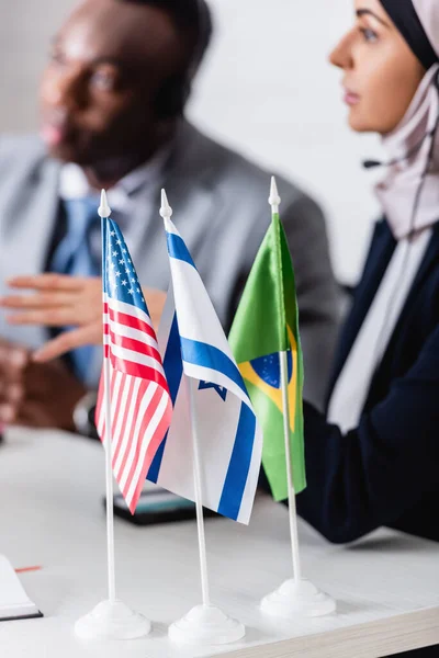 Focalizzazione selettiva di bandiere statunitensi, israeliane e brasiliane presso partner commerciali arabi e afroamericani su sfondo sfocato — Foto stock