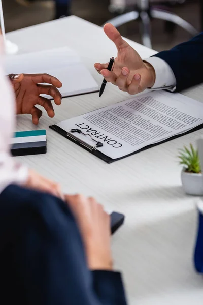 Cropped view of interracial business partners gesturing during discussion of contract, blurred foreground — Stock Photo