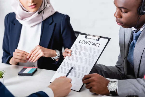 Vista recortada del intérprete apuntando con pluma en contrato cerca de socios comerciales afroamericanos y árabes - foto de stock