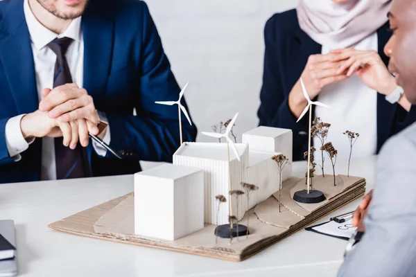 Partial view of multicultural business partners near model of alternative power station, blurred foreground — Stock Photo