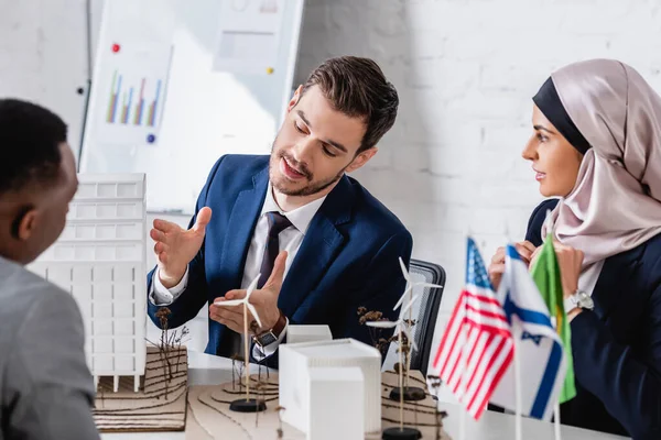 Traduttore indicando i modelli di costruzione e la stazione di energia verde vicino partner arabi e afro-americani, primo piano sfocato — Foto stock