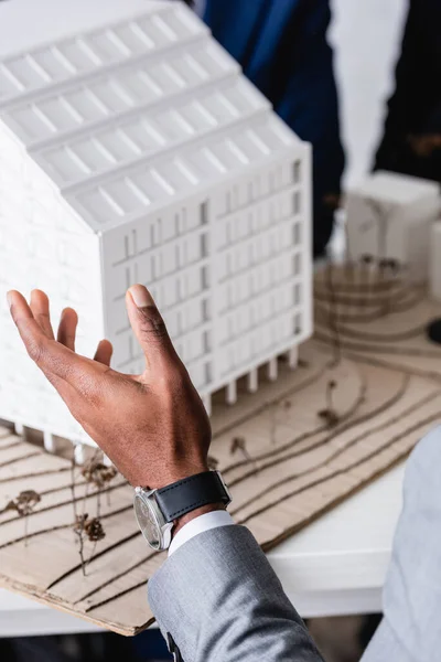 Partial view of african american businessman pointing with hand at building model, blurred background — Stock Photo