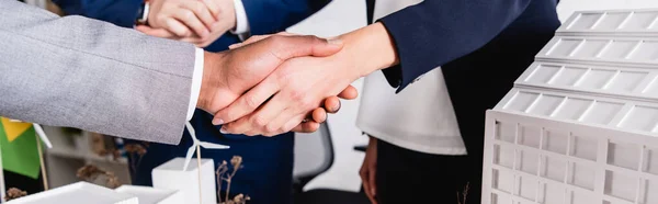 Vista ritagliata di afro-americano uomo d'affari che stringe la mano con la donna d'affari vicino al modello di costruzione, banner — Foto stock