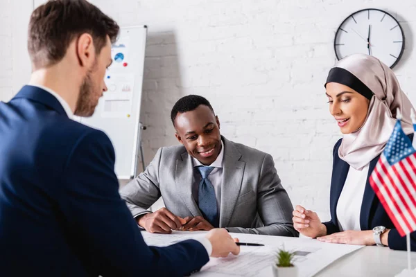 Fröhliche afrikanisch-amerikanische und arabische Geschäftspartner, die auf verschwommenem Vordergrund eine Blaupause in der Nähe des Übersetzers betrachten — Stockfoto