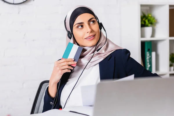 Intérprete arábico sorridente em fones de ouvido segurando tradutor digital com símbolo de bandeira uae, foreground borrado — Fotografia de Stock