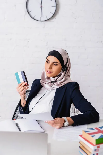 Arabian interpreter holding document and digital translator with uae flag emblem near dictionaries on blurred foreground — Stock Photo