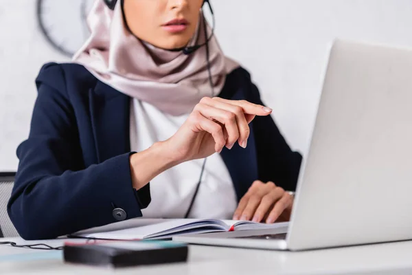 Vue recadrée de l'interprète arabe pointant avec le doigt près de l'ordinateur portable et le traducteur numérique sur le premier plan flou — Photo de stock