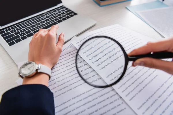 Cropped view of translator holding magnifier glass near documents with english text, blurred foreground — Stock Photo