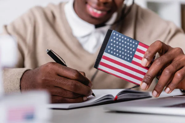 Foco seletivo do tradutor digital com EUA bandeira emblema perto de Africano americano intérprete escrita em fundo borrado, visão recortada — Fotografia de Stock