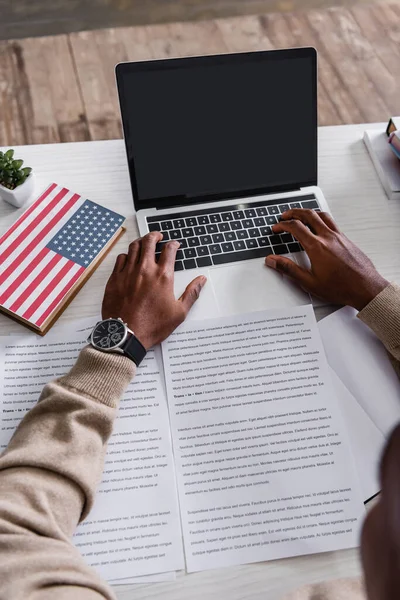 Vista recortada do intérprete americano africano que traduz documentos perto do portátil e do dicionário com bandeira dos EUA na tampa — Fotografia de Stock