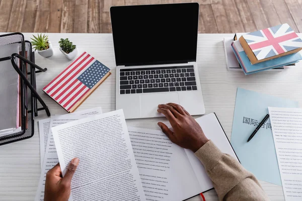Visão parcial do tradutor americano africano trabalhando com documentos perto de laptop e dicionários com EUA e grandes bandeiras de britain em capas — Fotografia de Stock