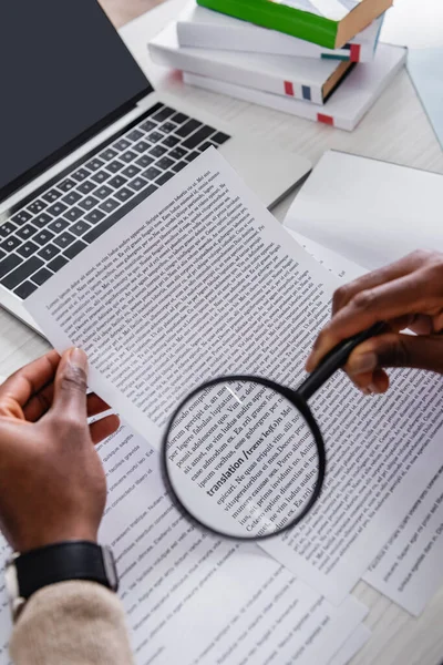 Partial view of african american translator holding magnifying glass near documents with english text — Stock Photo