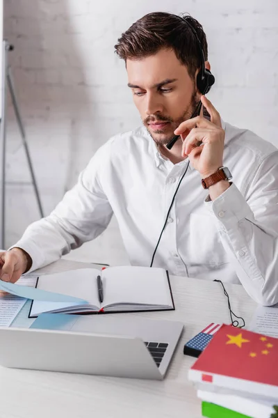 Young interpreter in headset holding document near digital translator and dictionaries on blurred foreground — Stock Photo