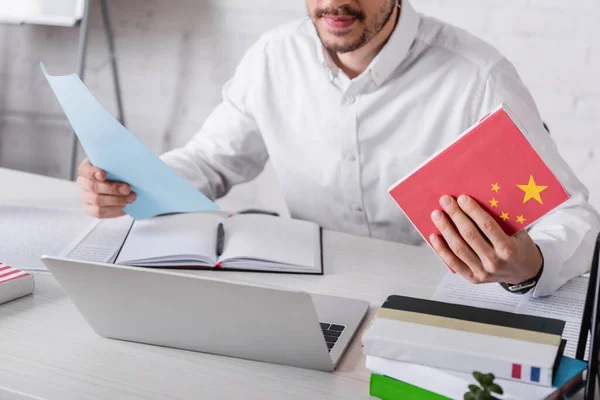 Partial view of translator holding chinese dictionary near notebook and laptop — Stock Photo