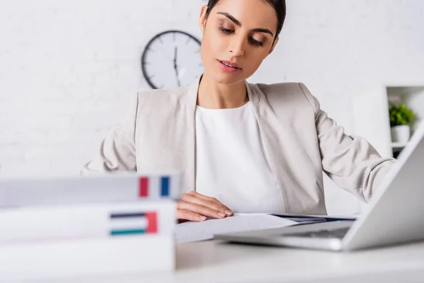 Focused translator working near laptop and dictionaries of french and arabian languages on blurred foreground — Stock Photo