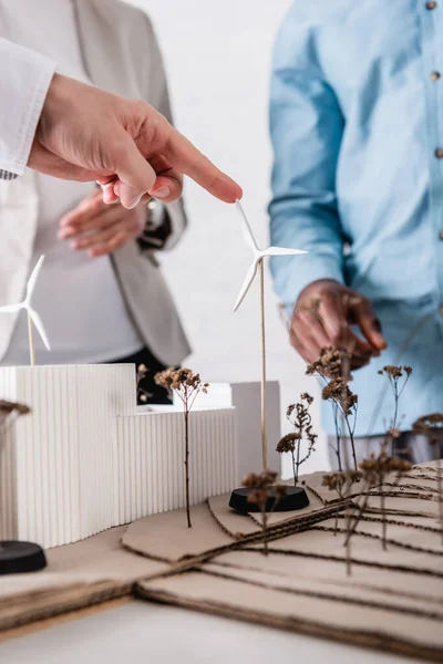 Abgeschnittene Ansicht eines Geschäftsmannes, der auf eine grüne Energiestation mit Windkraftanlagen in der Nähe multikultureller Partner zeigt, selektiver Fokus — Stockfoto