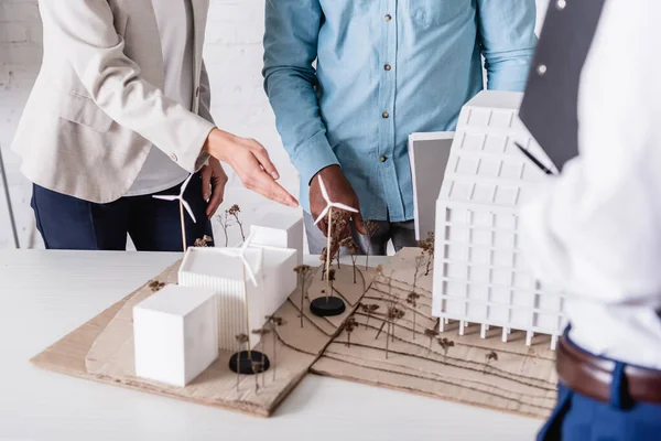 Partial view of businesswoman pointing at alternative power station model near multicultural business partners, blurred foreground — Stock Photo