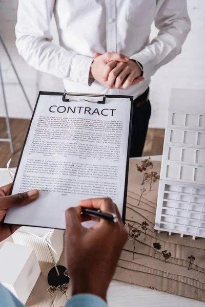 Teilansicht eines afrikanisch-amerikanischen Geschäftsmannes bei Vertragsunterzeichnung in der Nähe von Geschäftspartner und Ökostromkraftwerk-Modell, verschwommener Hintergrund — Stockfoto